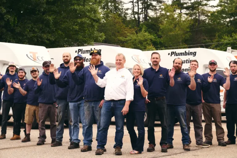 A group of workers in matching uniforms stands outdoors, waving at the camera, with branded service vans in the background.