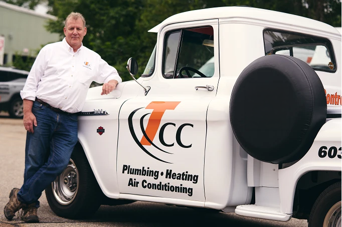 A man in a white shirt stands next to a white truck labeled "TCC Plumbing • Heating • Air Conditioning" in large letters on the door.